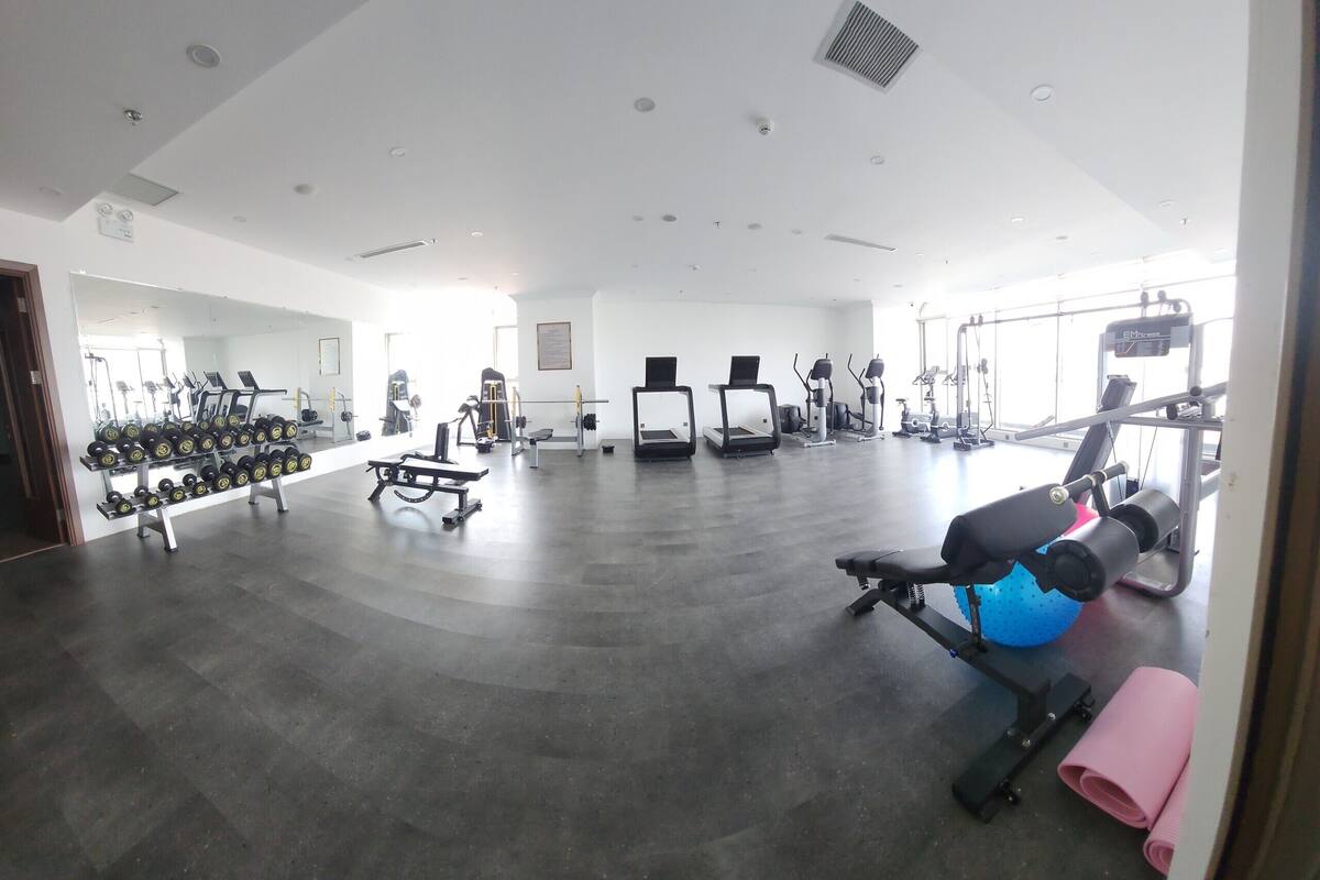 Un gimnasio con diverso equipo de ejercicio, incluyendo cintas de correr, mancuernas y una máquina de remo.