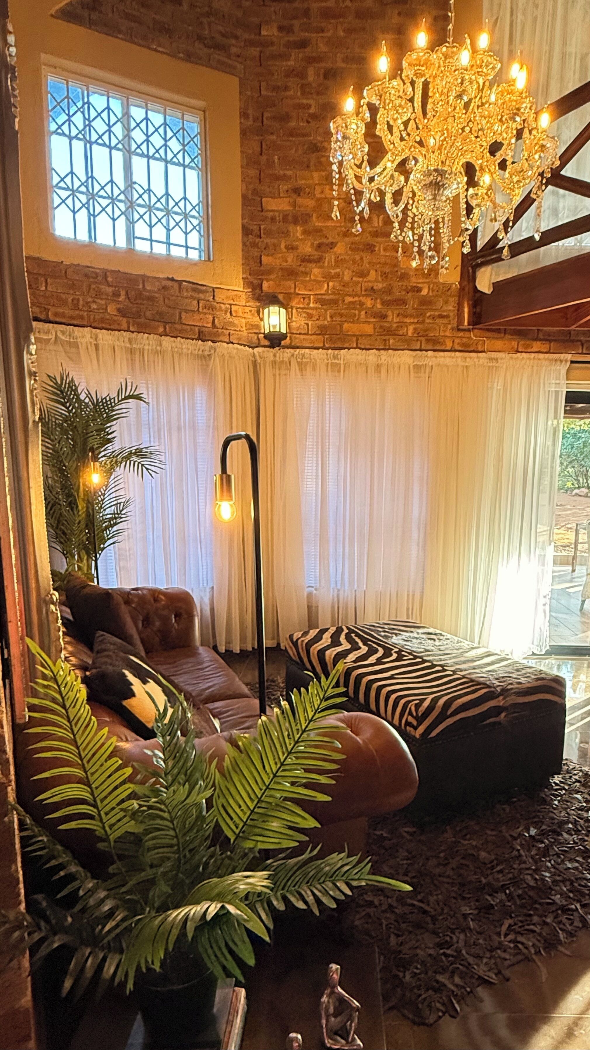 A cozy living room with a brick wall, a large window with bars, a chandelier, a sofa, a zebra-patterned ottoman, and a floor lamp.
