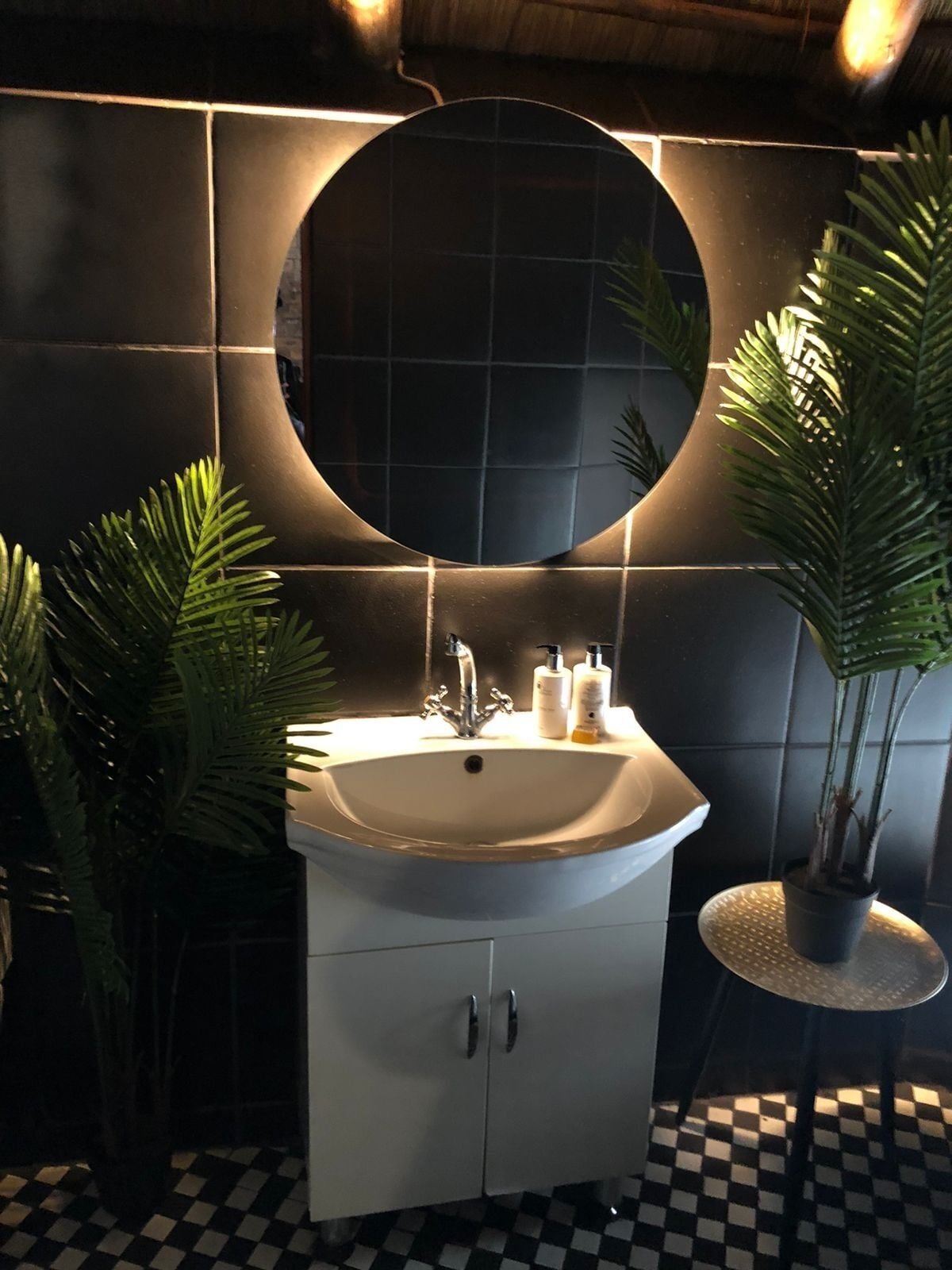 A bathroom with a white sink, a round mirror, and two potted plants.