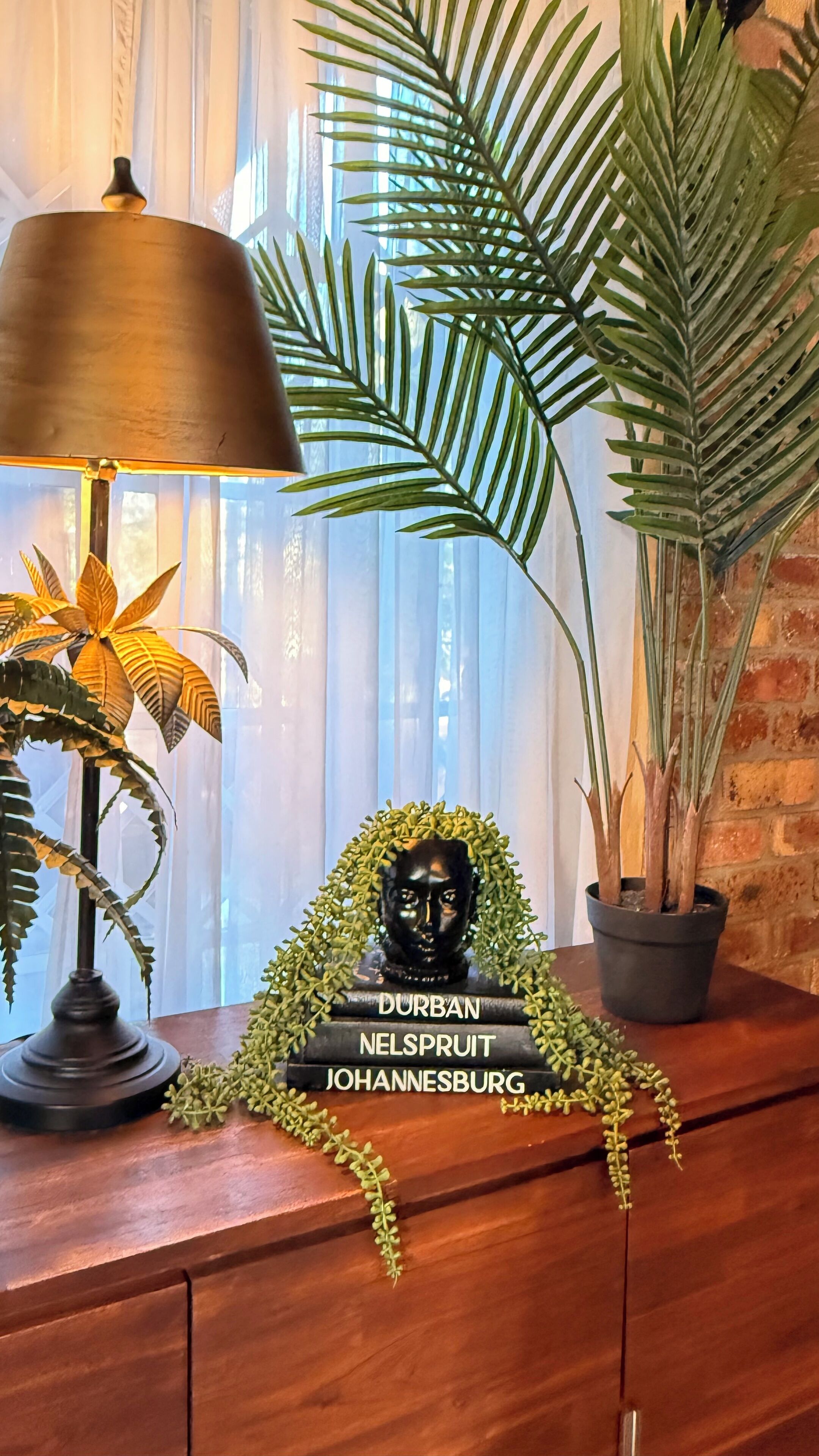 Een houten tafel met een lamp, een potplant en een borstbeeld met tekst.