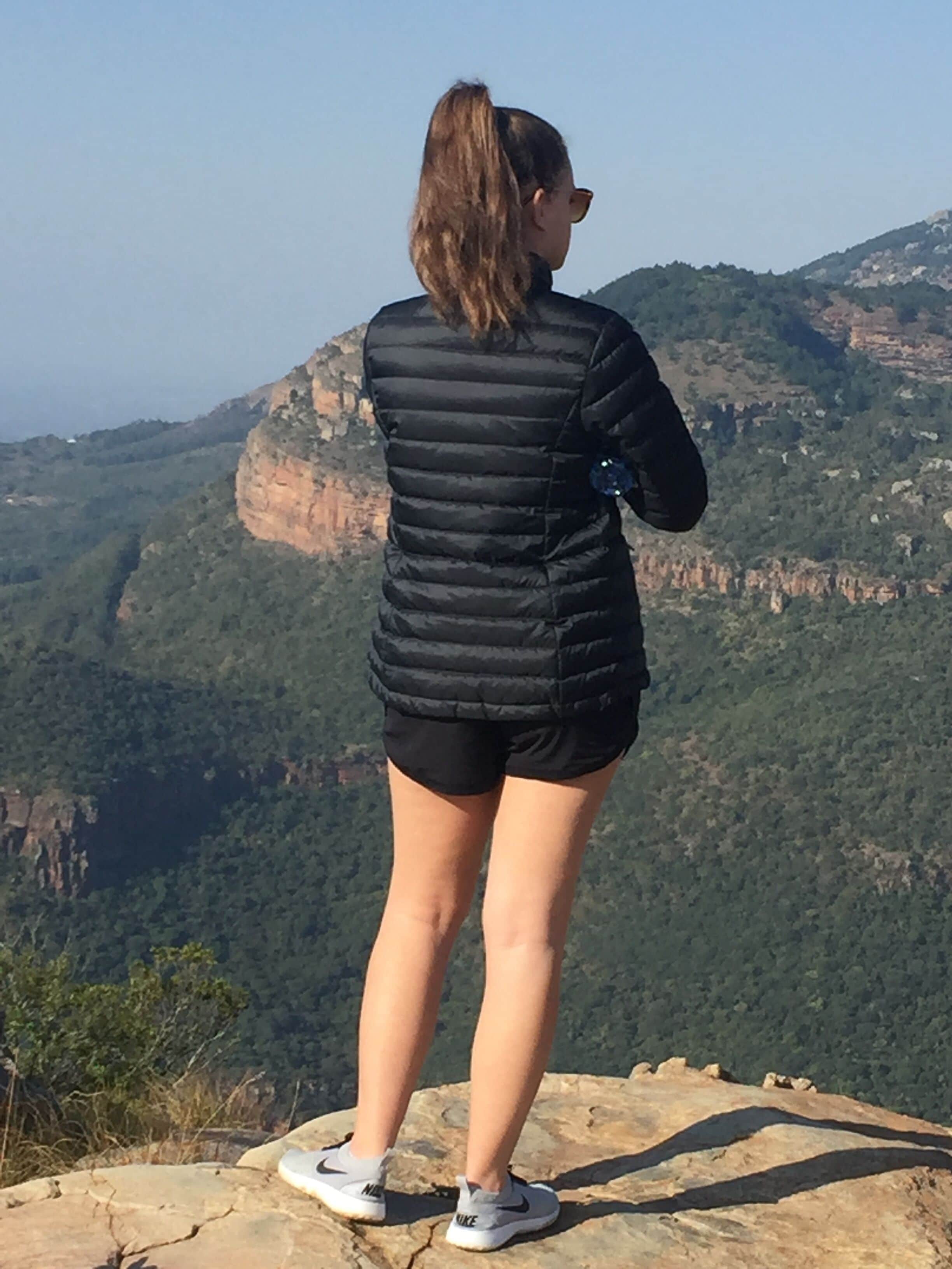 Una persona está de pie sobre un afloramiento rocoso con vistas a un paisaje montañoso.