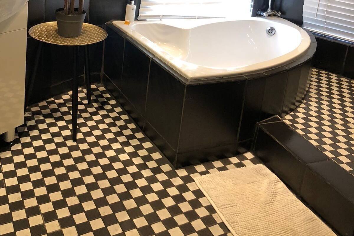 A modern bathroom with a checkered floor, a large bathtub, a potted plant, and a white sink.