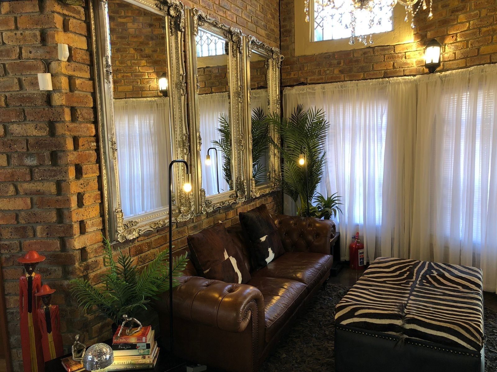 A cozy living room with a brick wall, a leather sofa, a zebra-patterned ottoman, and large mirrors.