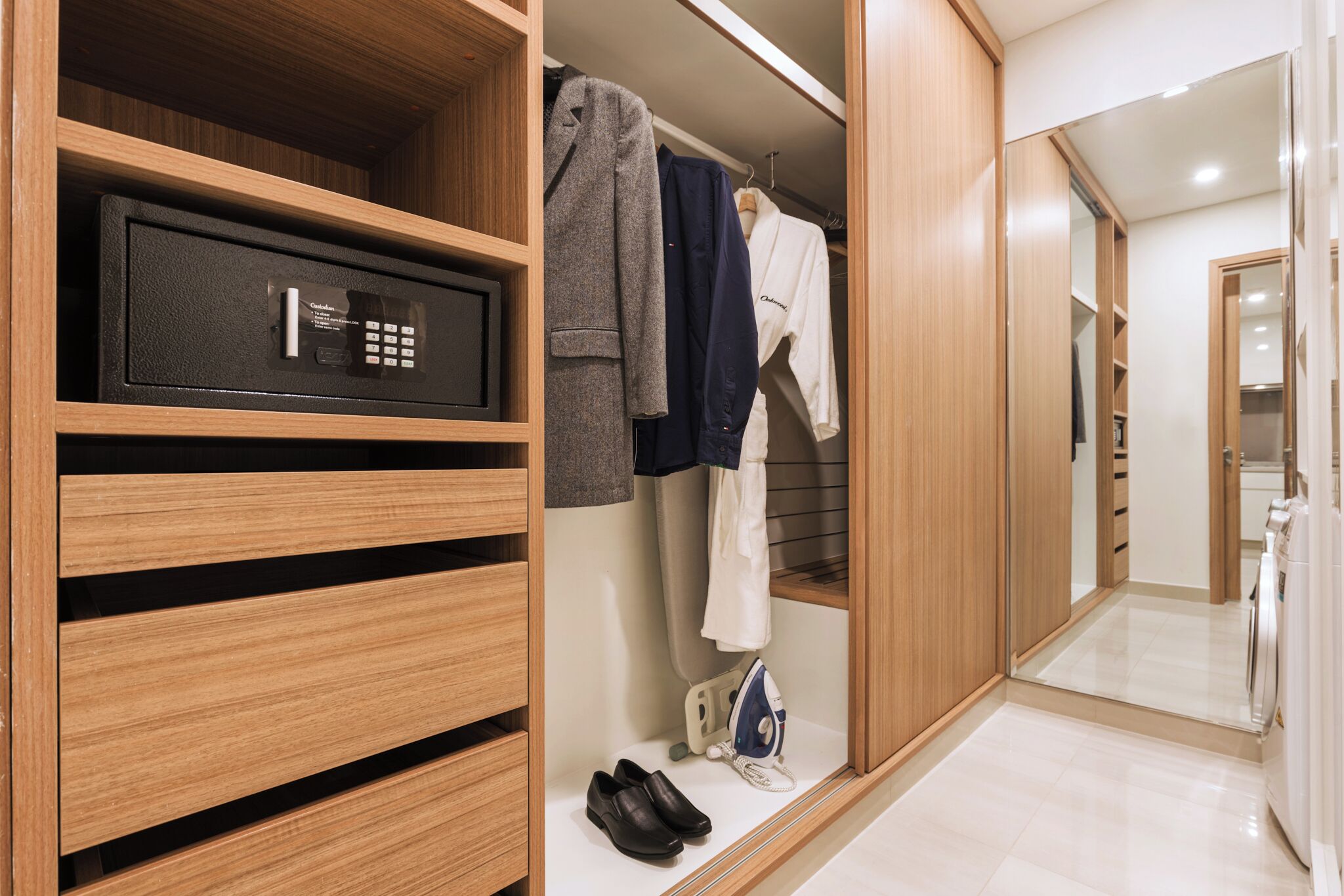 Un dressing avec un coffre-fort intégré, des vêtements suspendus, une planche à repasser et une paire de chaussures.
