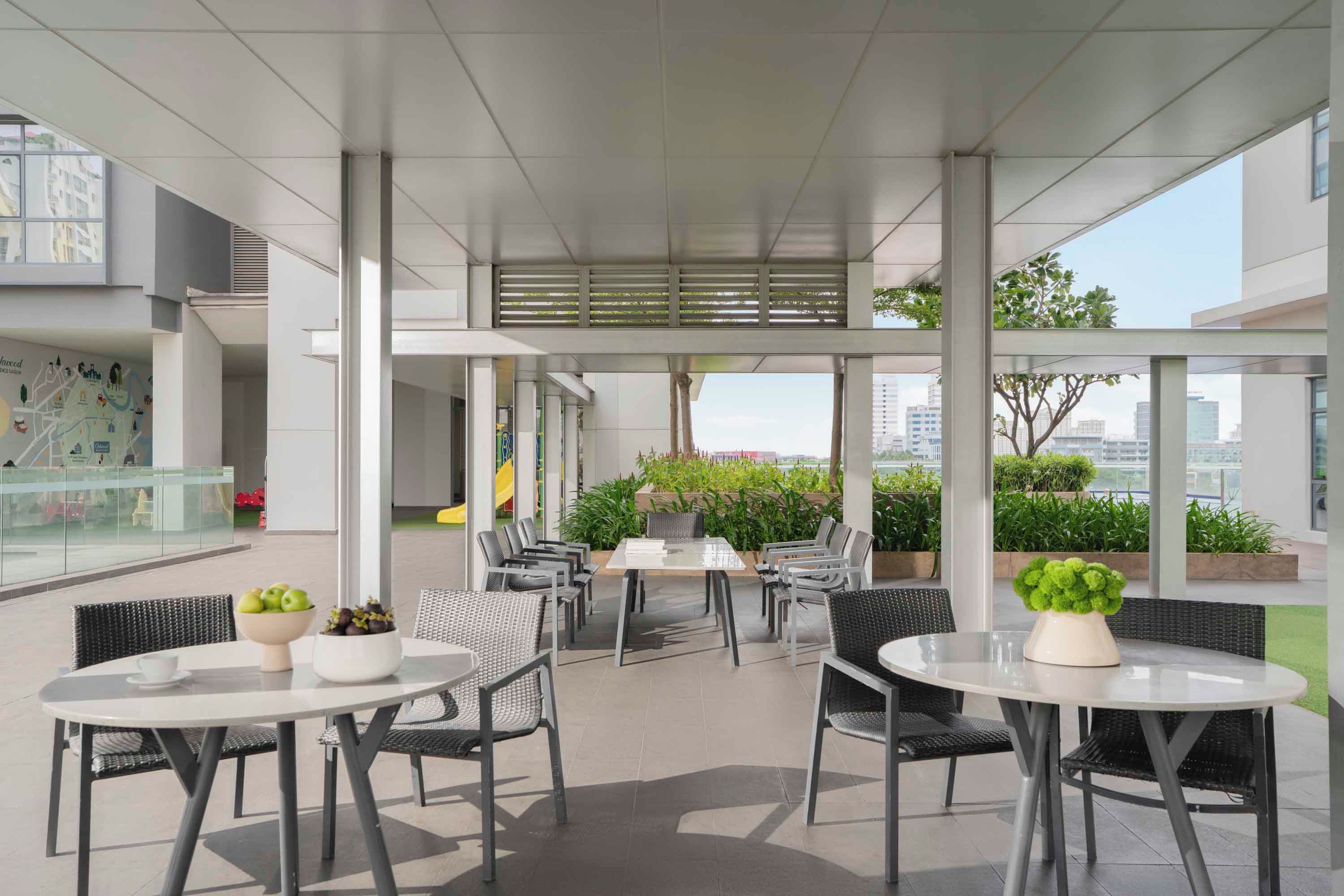 An outdoor seating area with tables and chairs, surrounded by glass railings and greenery.