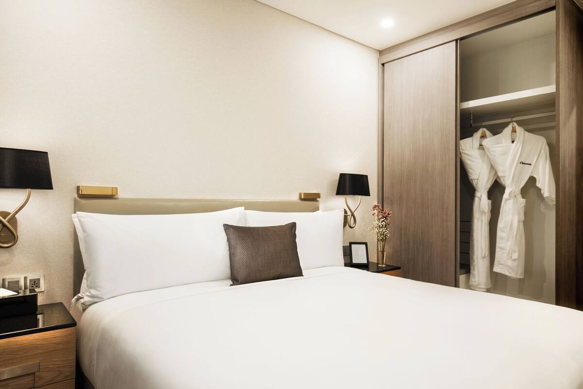 Una habitación de hotel con una cama grande, mesitas de noche, un armario y un espejo.