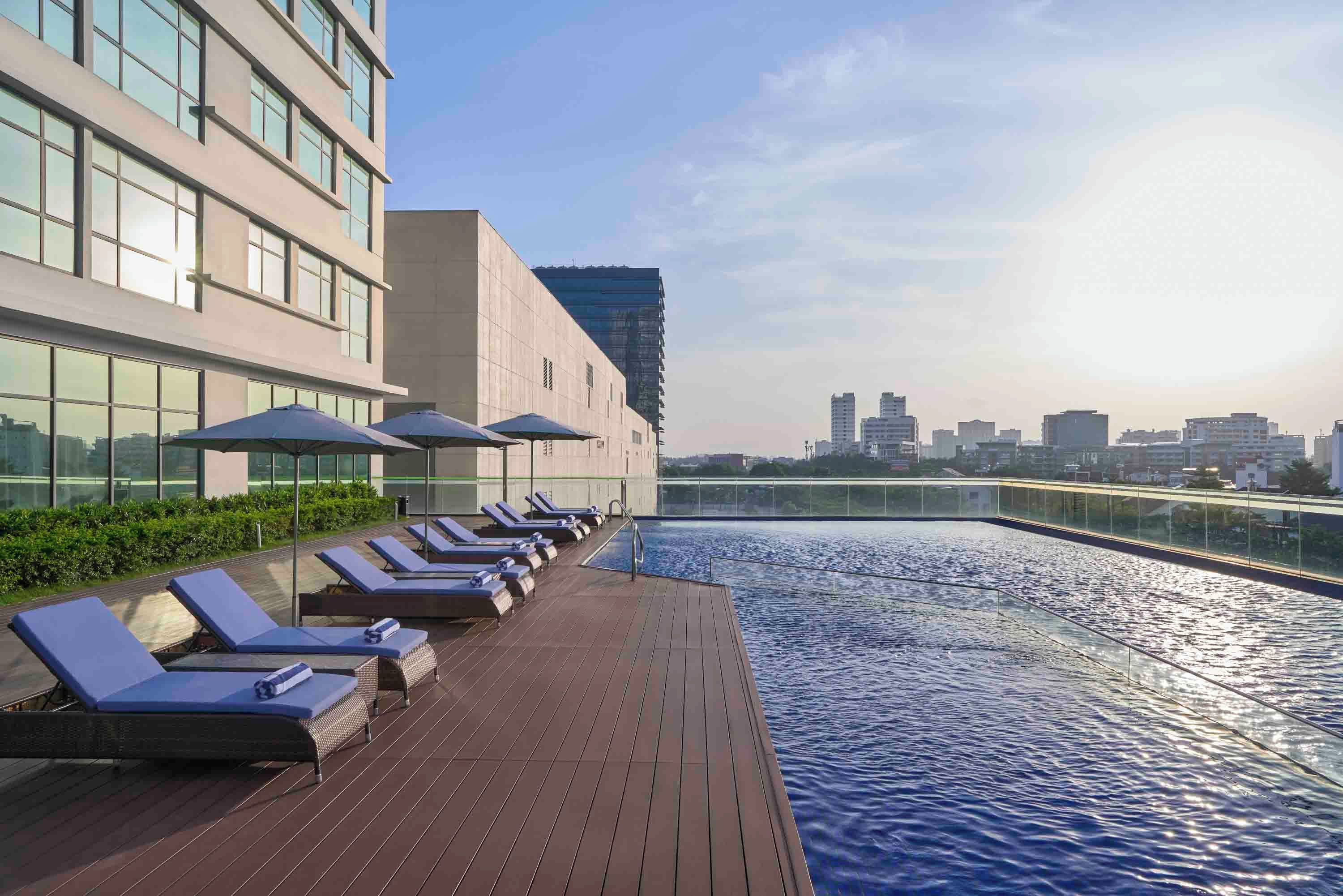 A rooftop pool with sun loungers and umbrellas, surrounded by a modern building with large windows.