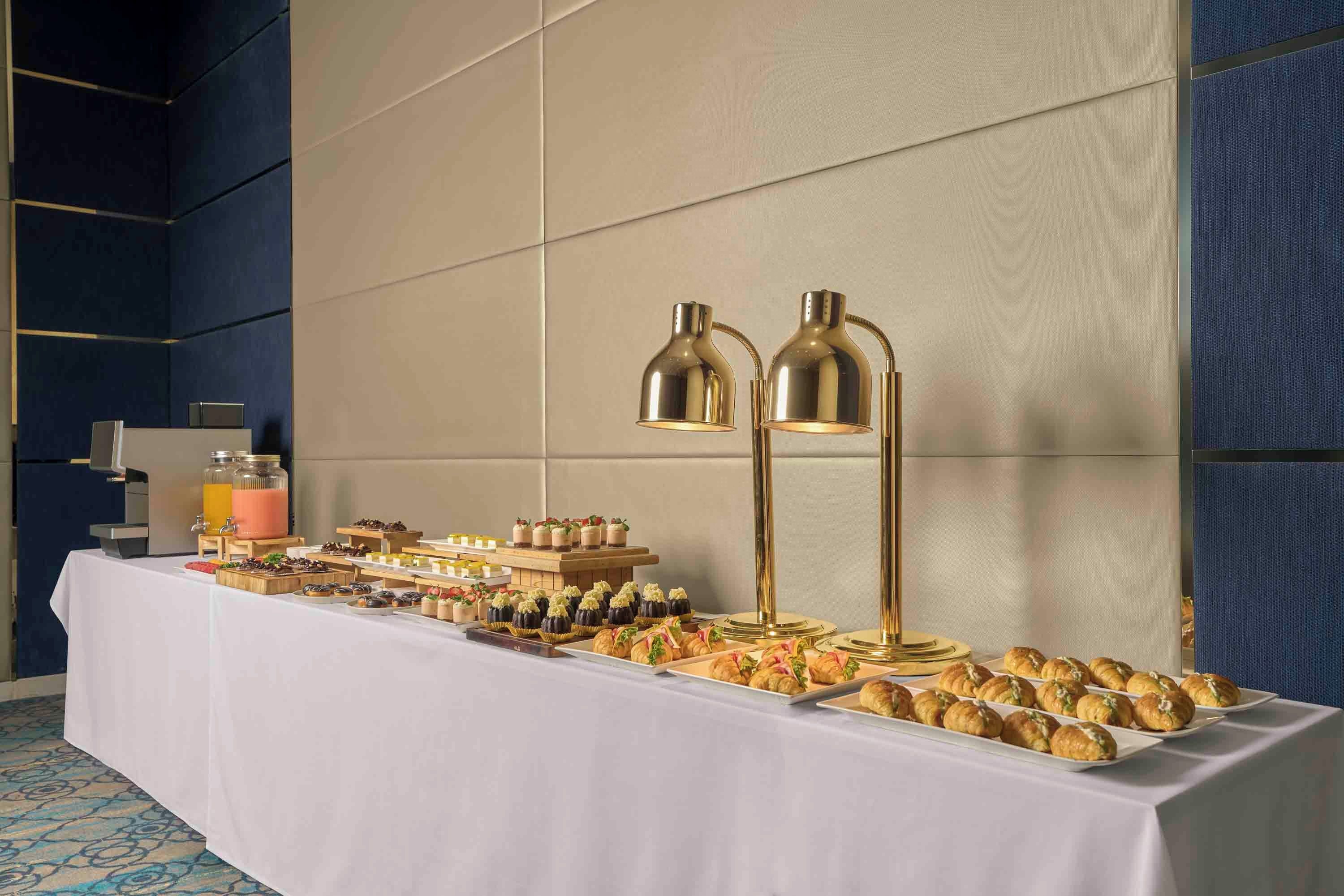 A buffet table with various food items and two gold-colored floor lamps.