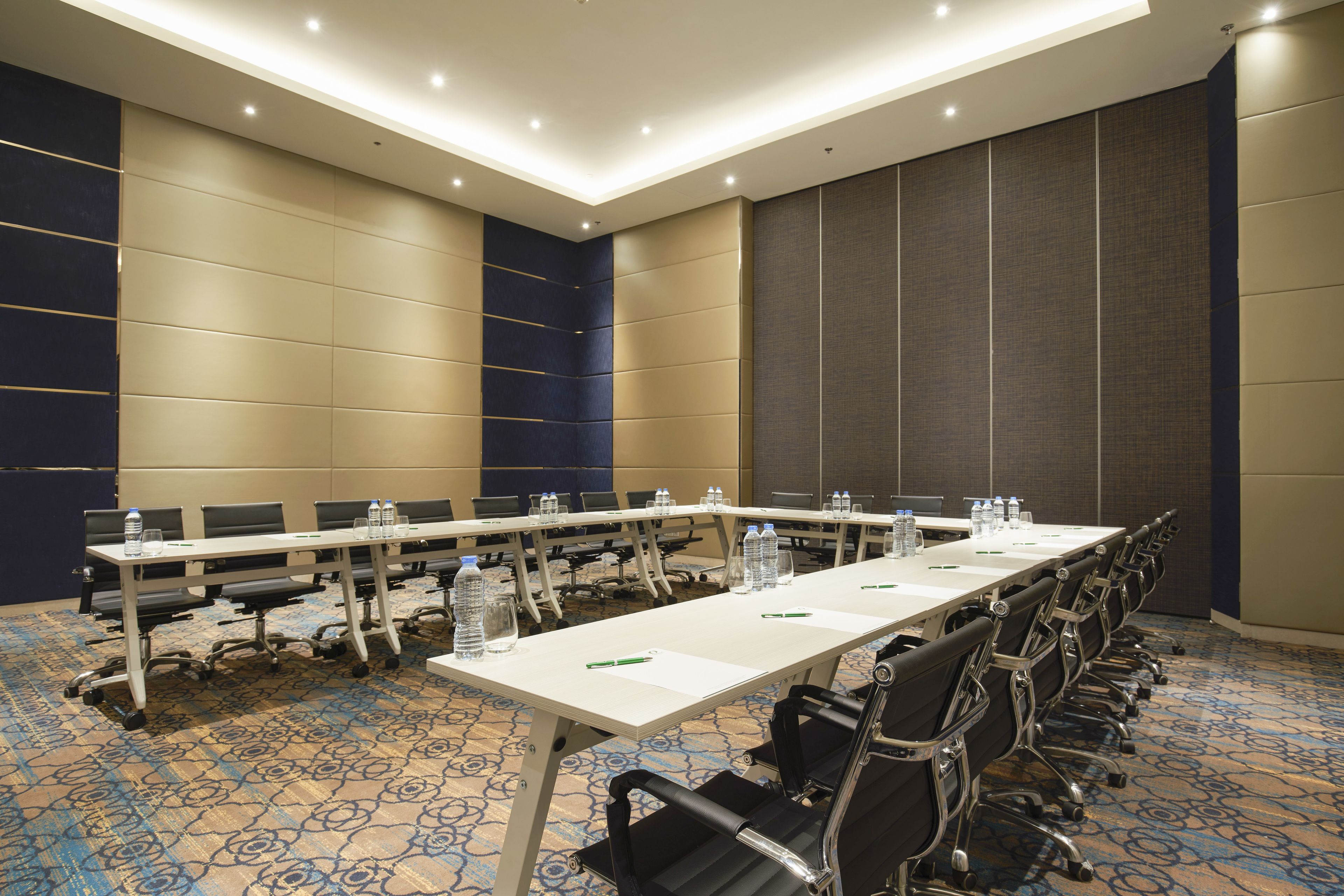 A conference room with a long table, chairs, water bottles, and a carpeted floor.