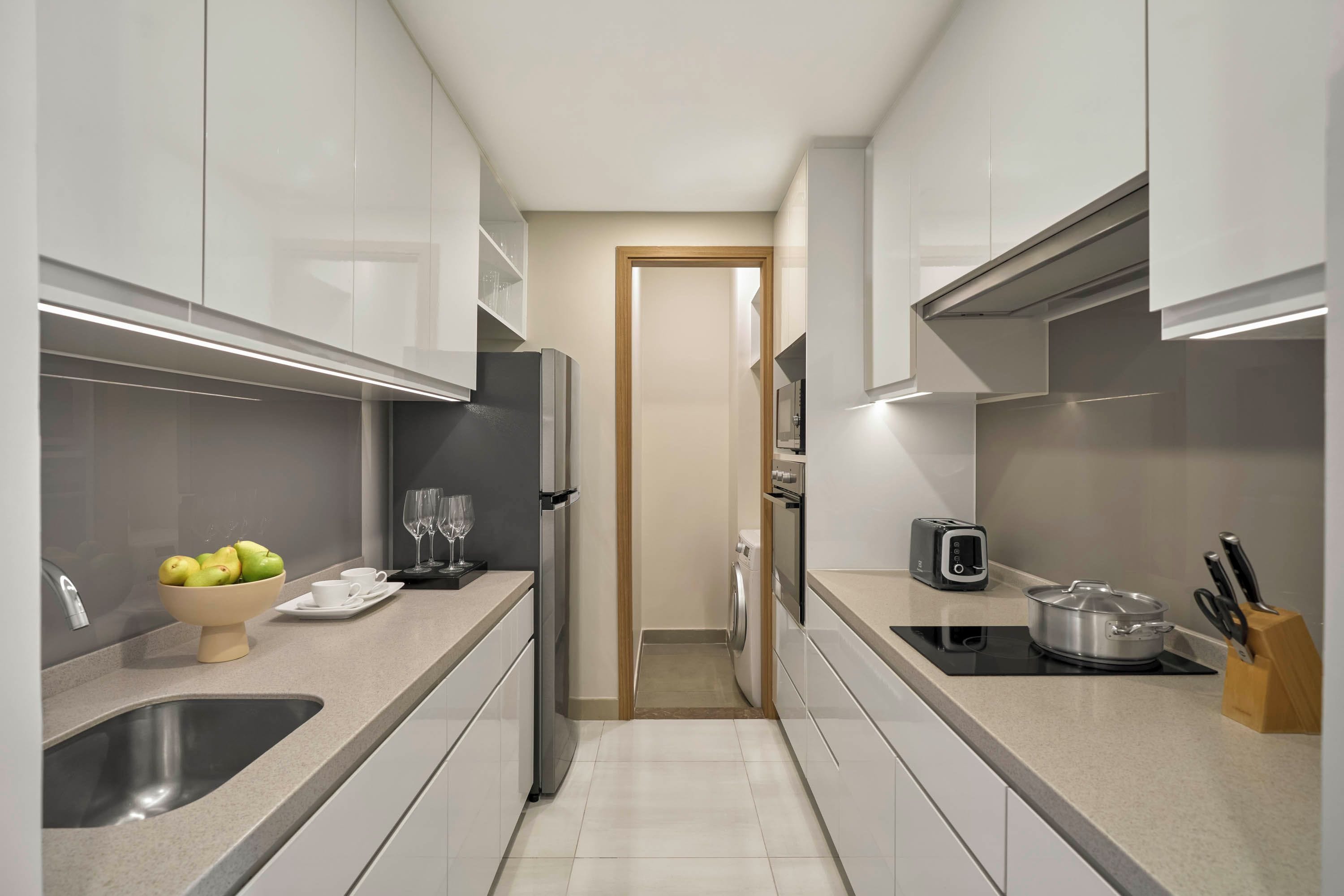 A narrow kitchen with white cabinets, a stainless steel sink, a bowl of fruit, and a toaster.