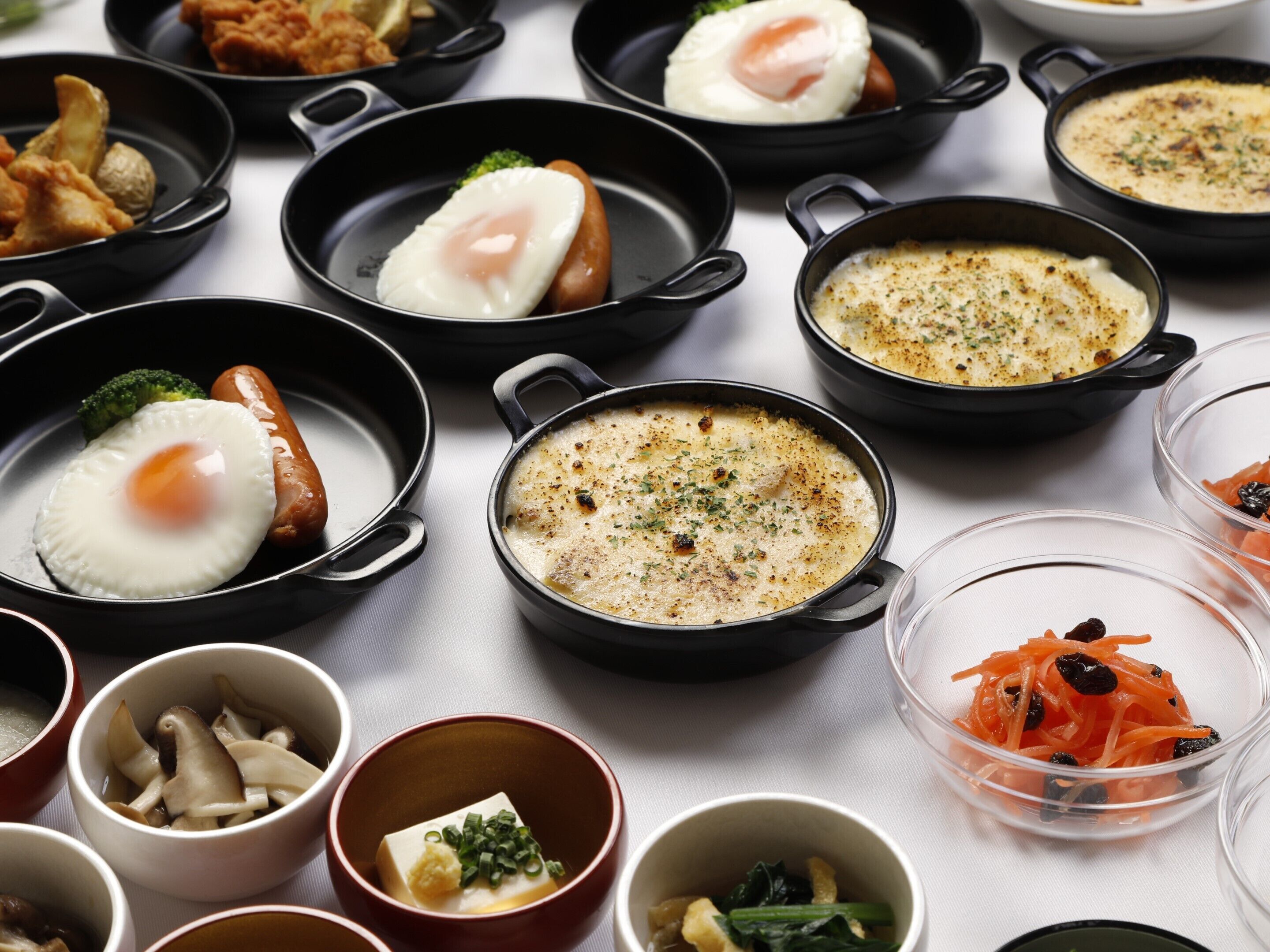 A variety of dishes in black pans, including fried eggs, sausages, and a creamy soup.