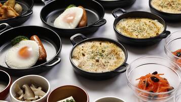 A variety of dishes in black pans, including fried eggs, sausages, and a creamy soup.