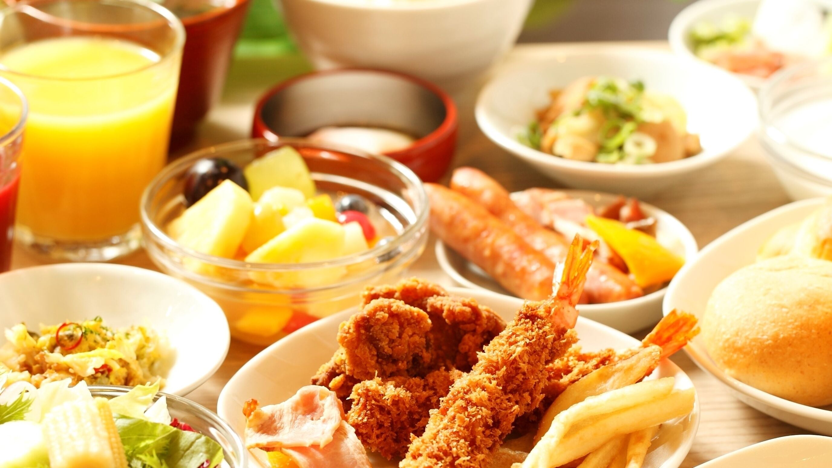 Una mesa con diferentes platos, incluyendo pollo frito, papas fritas y un bol de fruta.