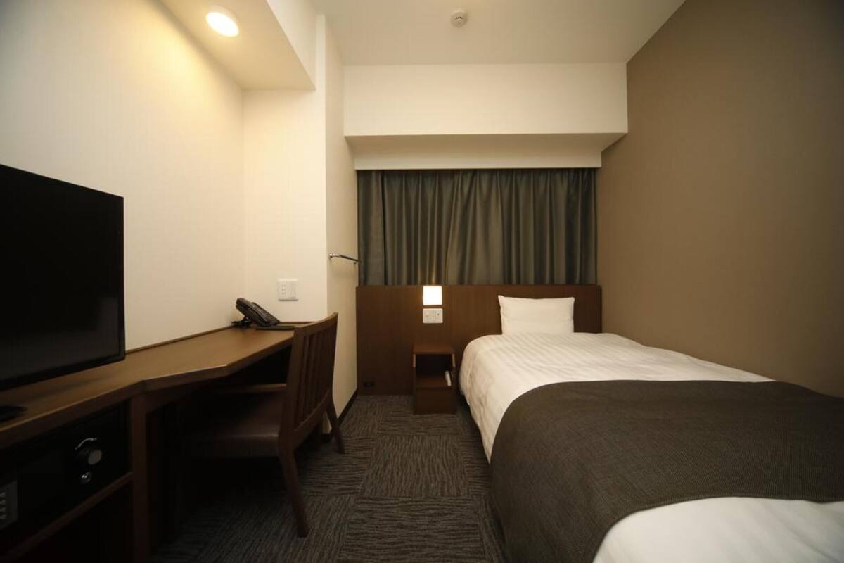 Ein Hotelzimmer mit einem Bett, einem Schreibtisch mit Fernseher und einem Nachttisch.