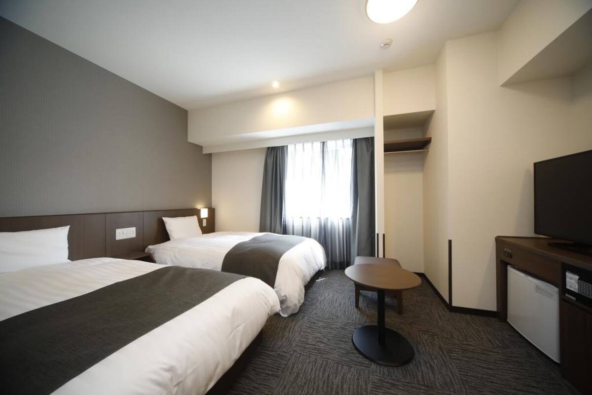 Ein Hotelzimmer mit zwei Betten, einem kleinen Tisch, einem Fernseher und einem Kleiderschrank.