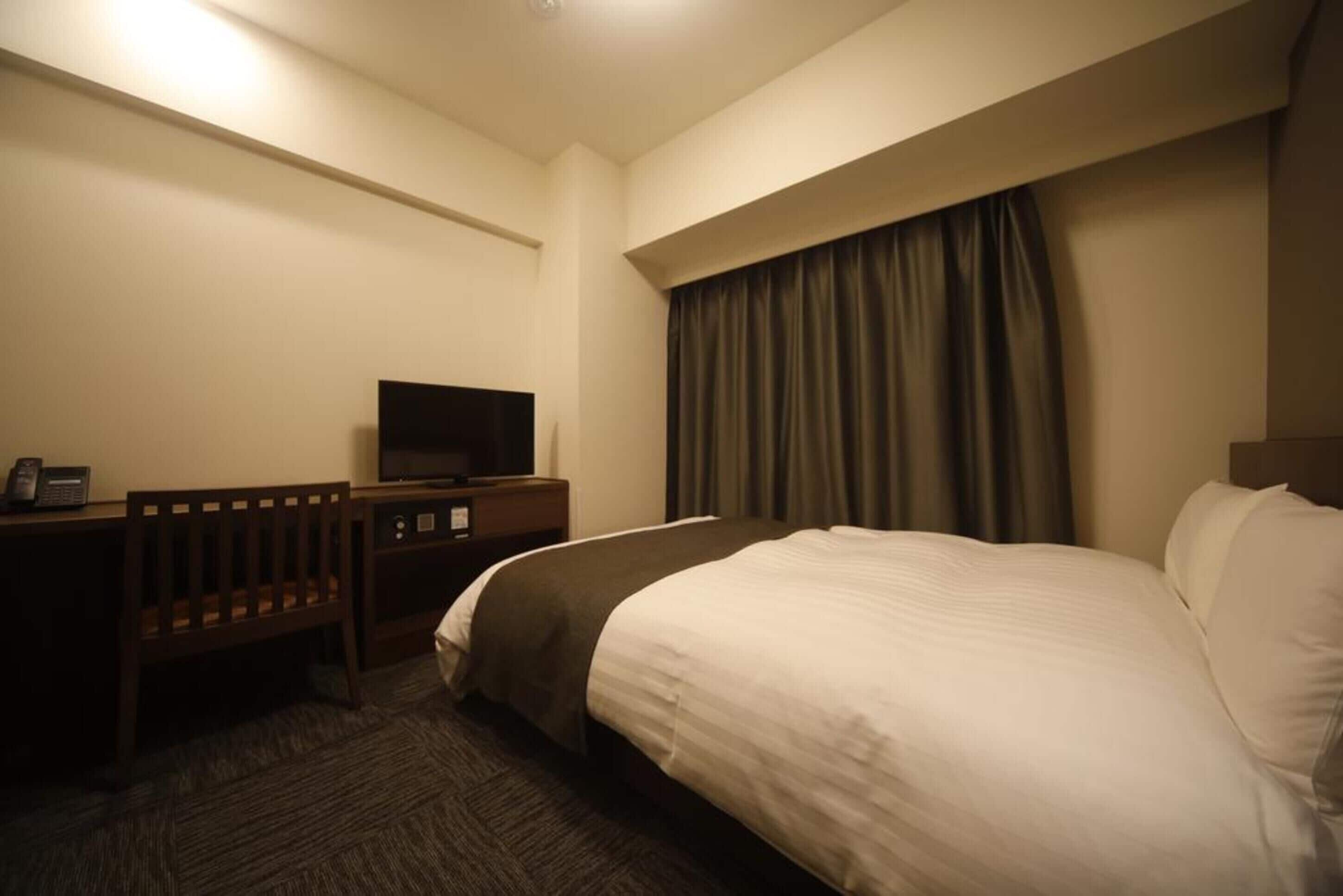 Una habitación de hotel con cama, escritorio con televisor y teléfono.
