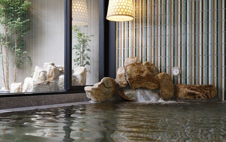 A water feature with rocks and a clock, set against a striped wall and a window with a plant.