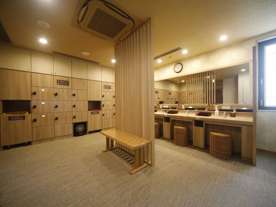 A hotel bathroom with wooden lockers, a bench, a sink area, and a clock on the wall.