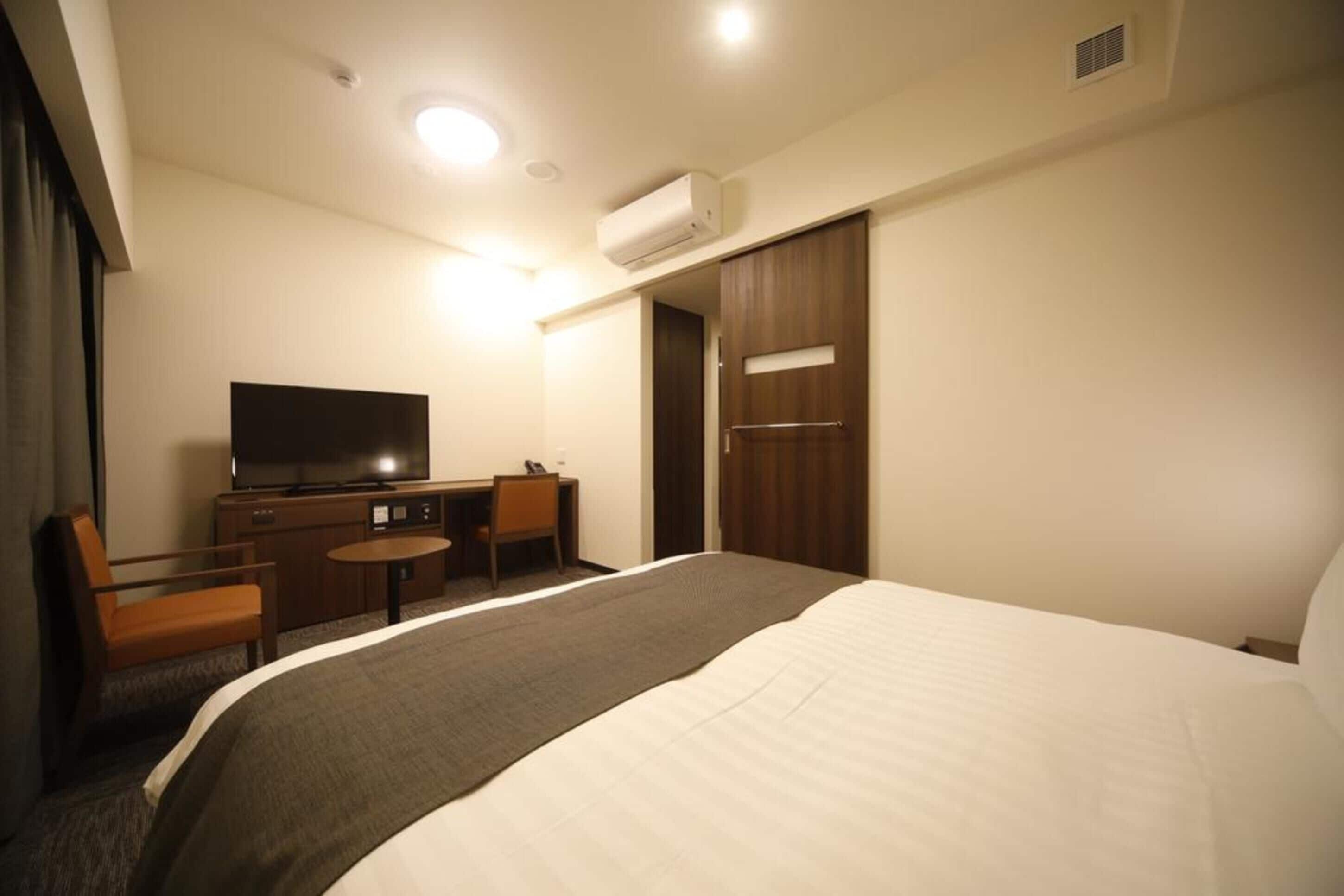 Una habitación de hotel con cama, escritorio, silla, televisor y armario.