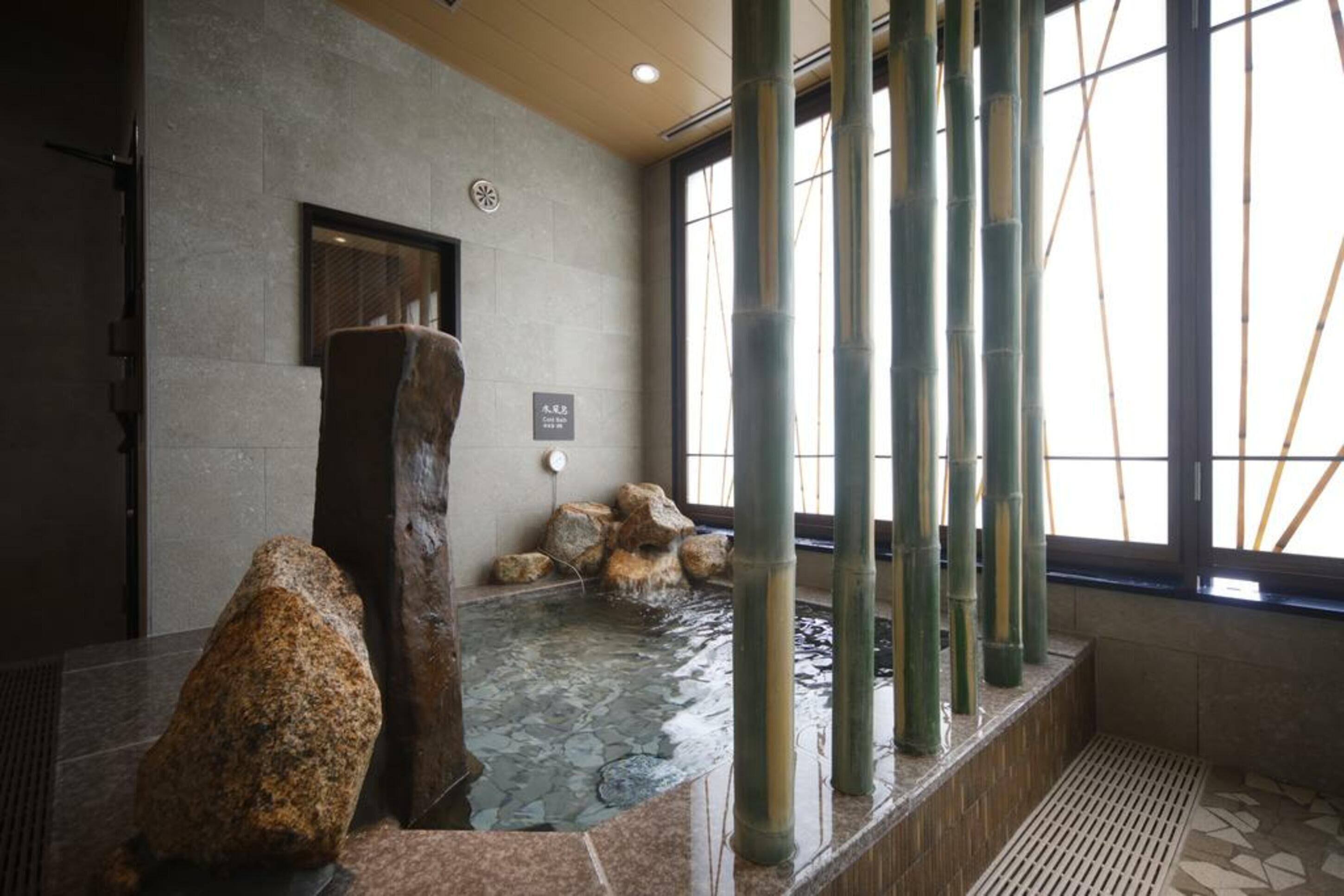 A spa area with a stone basin, bamboo pillars, and a stone wall.