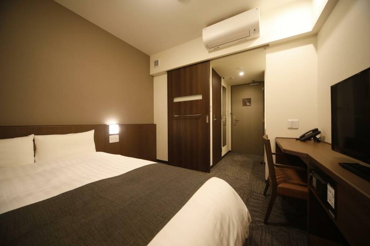 Ein Hotelzimmer mit einem großen Bett, einem Schreibtisch mit Stuhl, einem Fernseher und einer Klimaanlage.