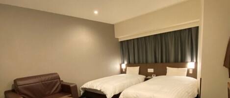 A hotel room with two beds, a brown leather sofa, a small round table, and a ceiling light.