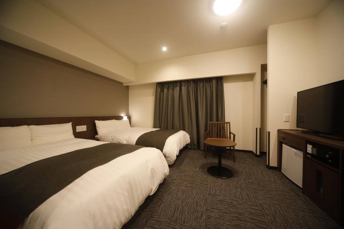 Ein Hotelzimmer mit zwei Betten, einem Fernseher, einem Schreibtisch und einem Sessel.