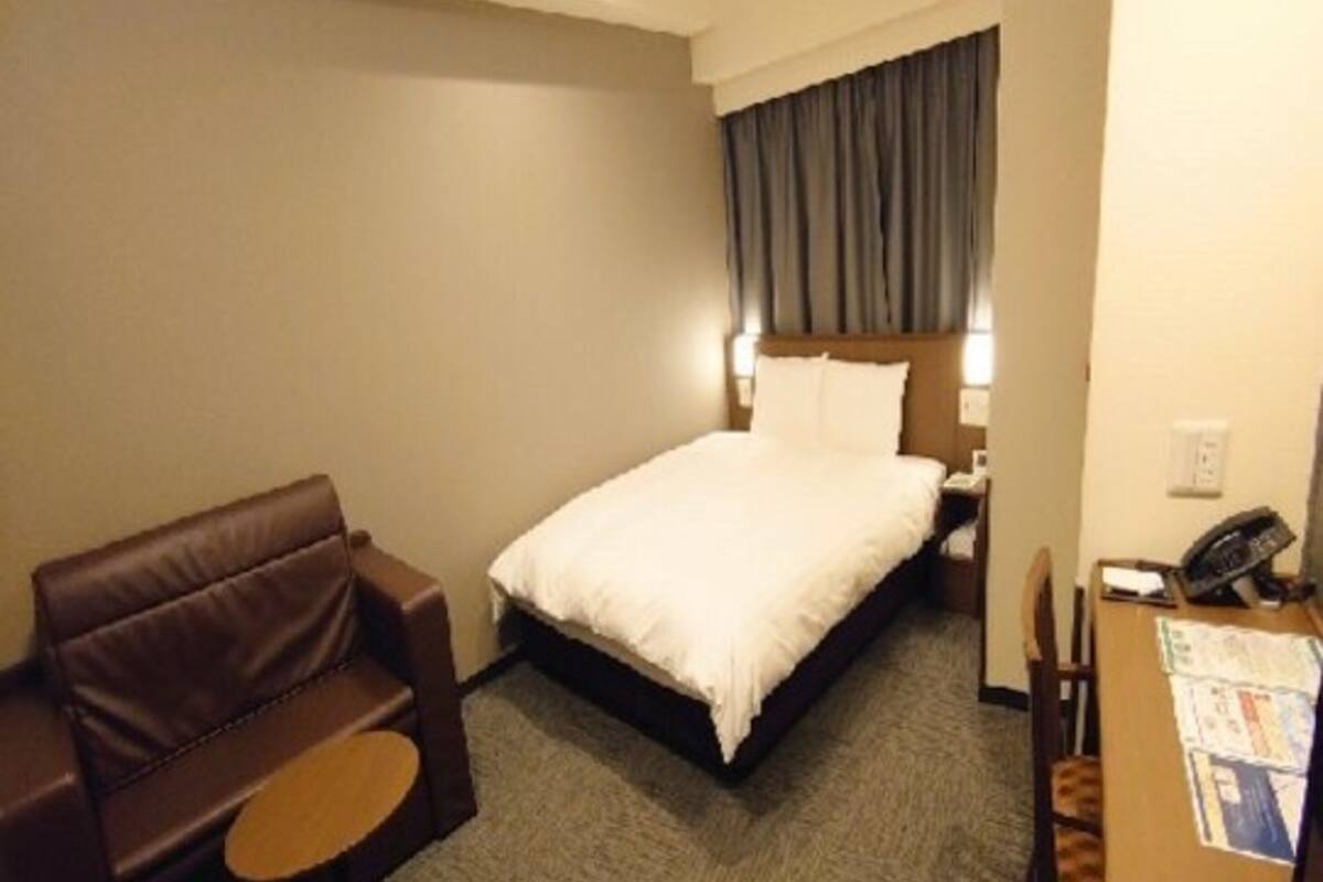 Ein Hotelzimmer mit einem Bett, einer braunen Ledersofa, einem kleinen runden Tisch und einem Schreibtisch mit Telefon.