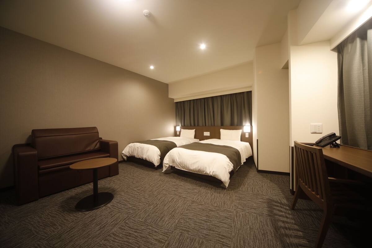 Ein Hotelzimmer mit einer Couch, zwei Betten, einem Schreibtisch und einem Telefon.