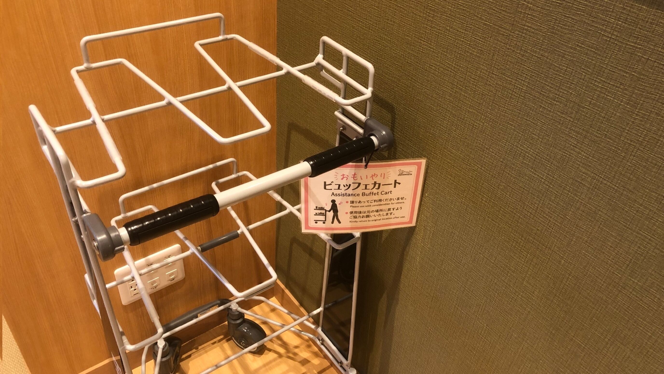 A metal cart with a sign in Japanese, likely for a buffet service, against a wooden wall.