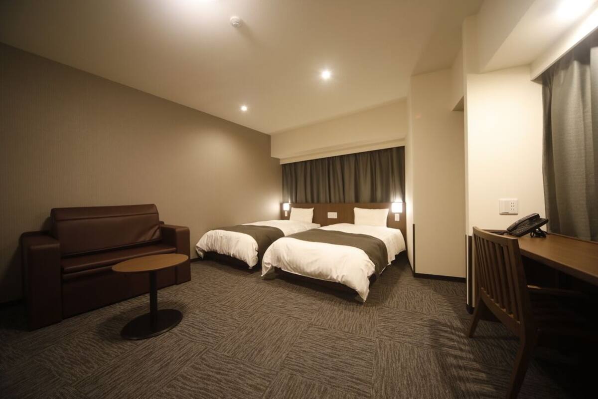 Ein Hotelzimmer mit zwei Betten, einem Sofa, einem kleinen Tisch und einem Schreibtisch mit Telefon.