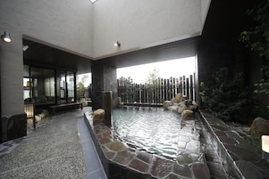 Un área de spa con una bañera de hidromasaje revestida de piedra, asientos y vistas a una valla de madera y follaje.