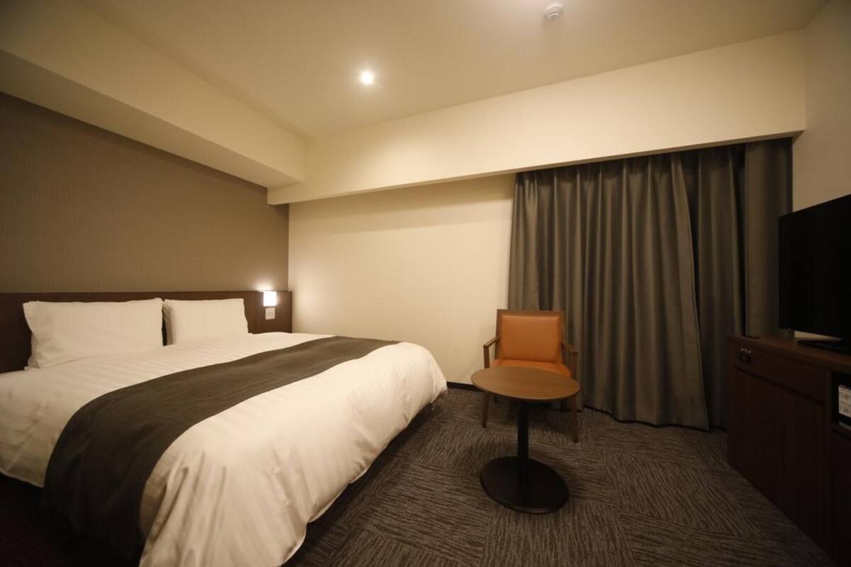 Ein Hotelzimmer mit einem großen Bett, einem Sessel, einem Fernseher und einem Vorhang.