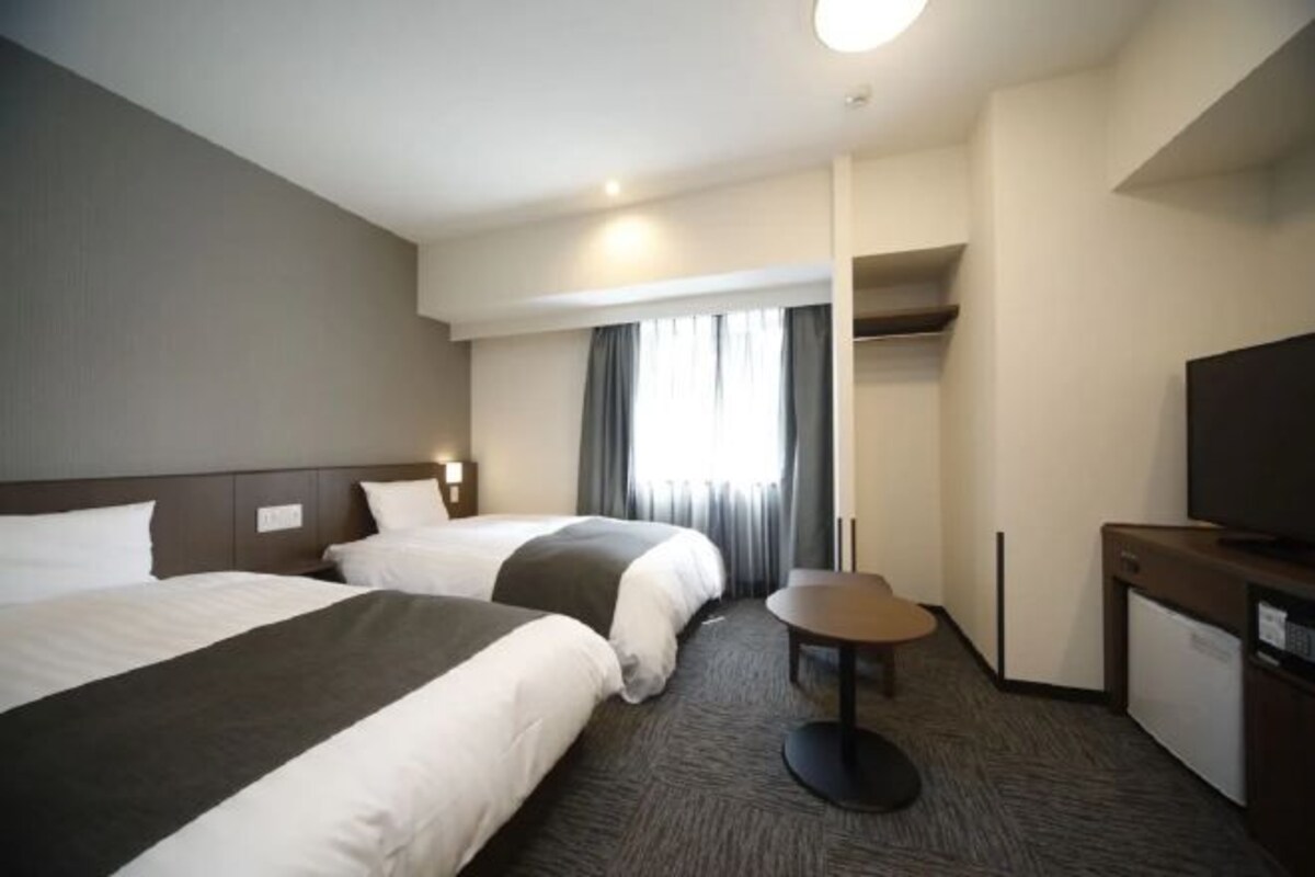 Een hotelkamer met twee bedden, een tafeltje, een televisie en een kledingkast.