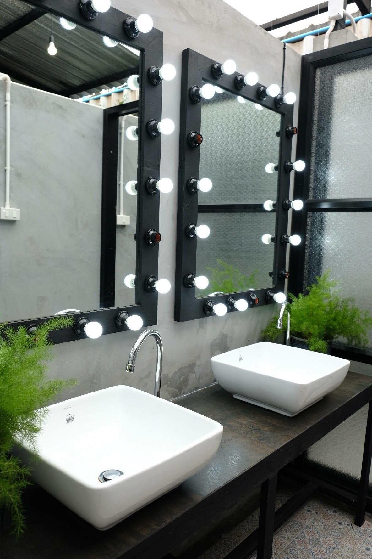 Ein Badezimmer mit zwei weißen Waschbecken, einem großen Spiegel mit Beleuchtung und einem Fenster.