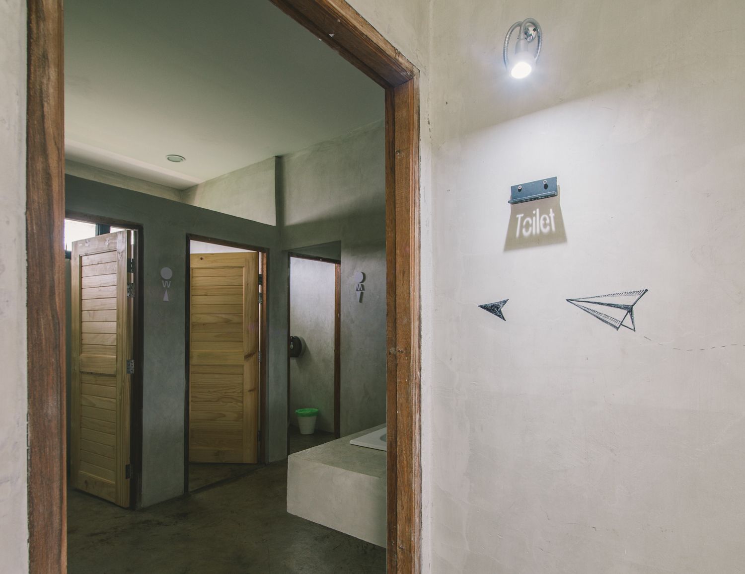 A hallway with wooden doors, a sign indicating a toilet, and a small trash bin.