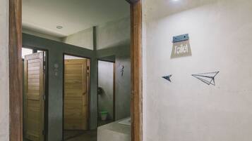 A hallway with wooden doors, a sign indicating a toilet, and a small trash bin.