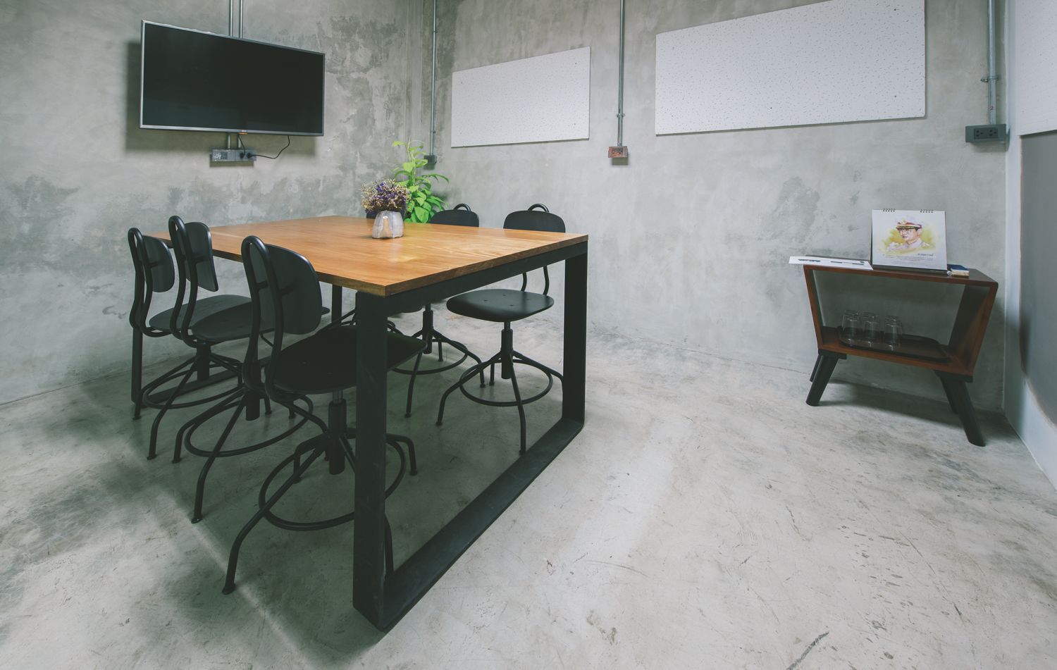 Una sala de conferencias con una mesa de madera, sillas negras, un televisor, pizarras blancas y un pequeño estante con vasos.
