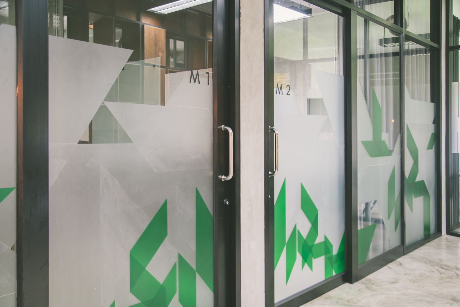 A modern office interior with glass partitions, metal handles, and geometric patterns.