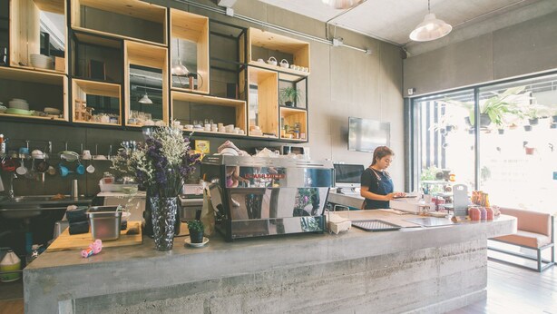 A modern cafe with a concrete counter, wooden shelves, and hanging plants.