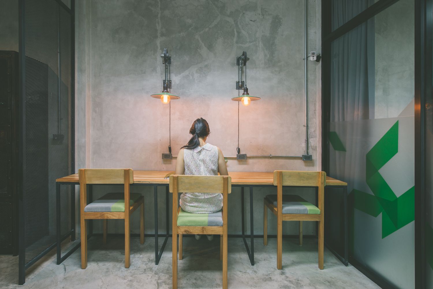 A room with a wooden table and chairs, a person seated at the table, and two hanging pendant lights.