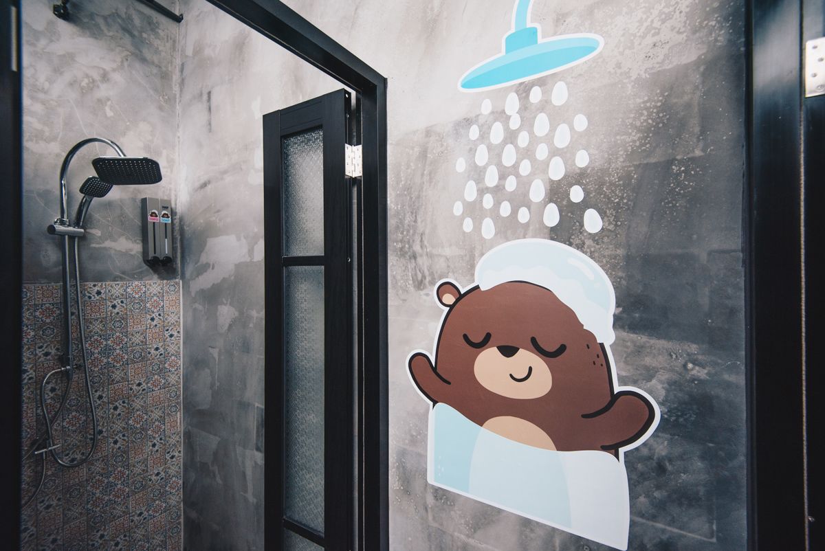 A bathroom with a shower, a towel rack, and a bear sticker on the wall.