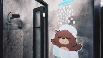 A bathroom with a shower, a towel rack, and a bear sticker on the wall.