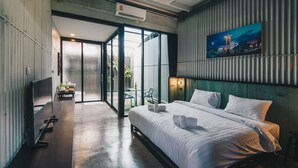 A modern hotel room with a large bed, a desk, and a view of the outdoor area.