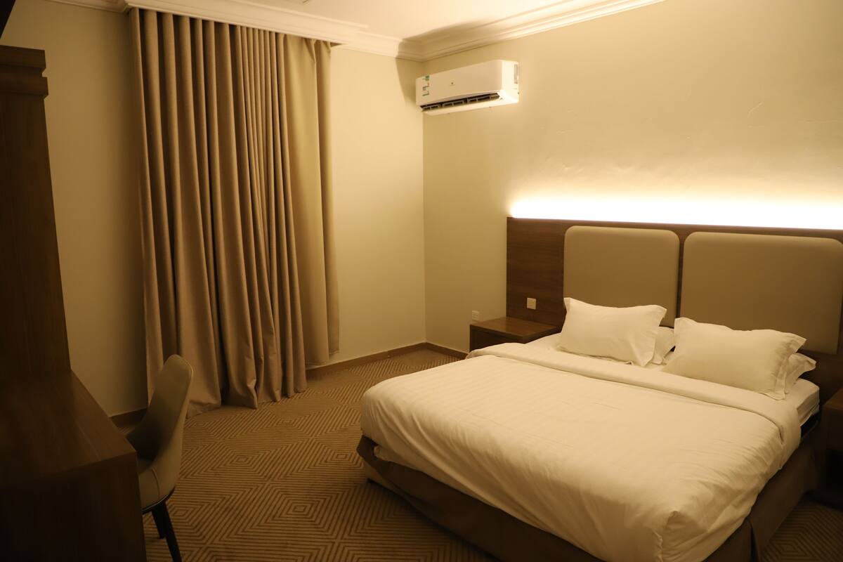 A hotel room with a large bed, a nightstand, a desk, and a chair.