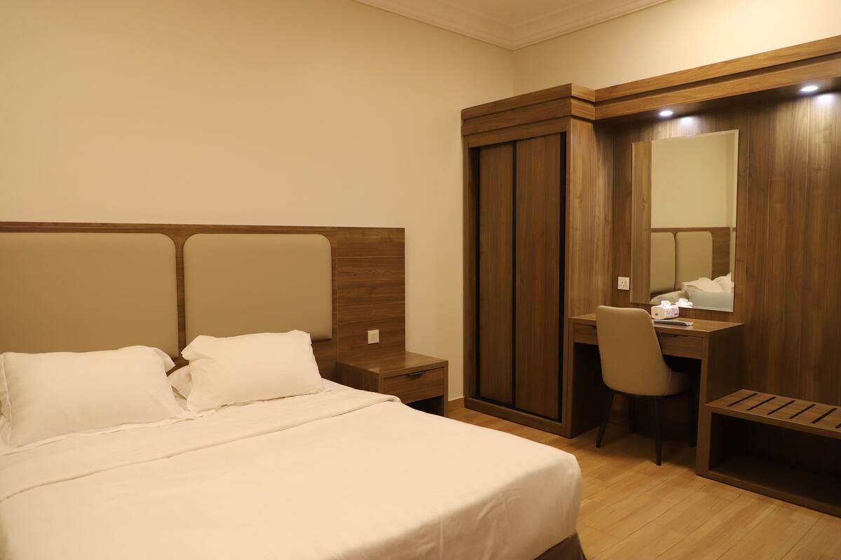 A hotel room with a bed, a desk, a chair, a wardrobe, and a mirror.