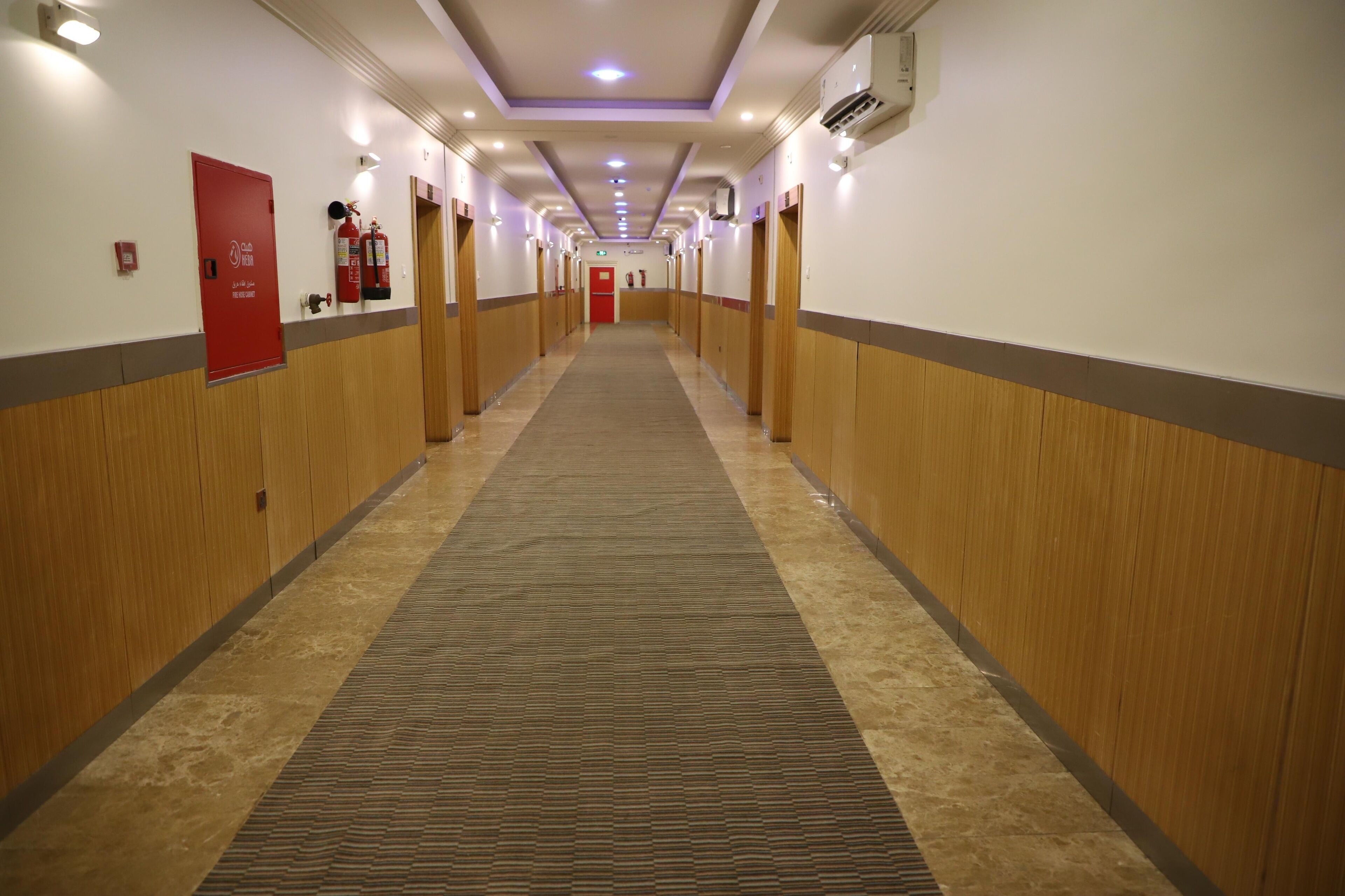 A hotel corridor with wooden paneling, a patterned carpet, and fire safety equipment.