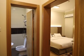 Et hotelværelse med bruser, toilet og en seng med sengegavl.