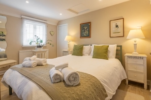 A hotel room with a large bed, two bedside tables, a window with blinds, a potted plant, and a painting on the wall.
