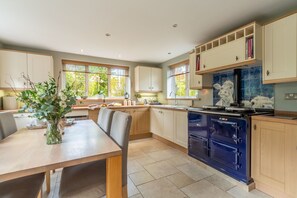 A modern kitchen with wooden cabinets, a blue stove, and a dining area with a table and chairs. - Cherry Cottage Ripe, nr Lewes , Sussex (nr Lewes)